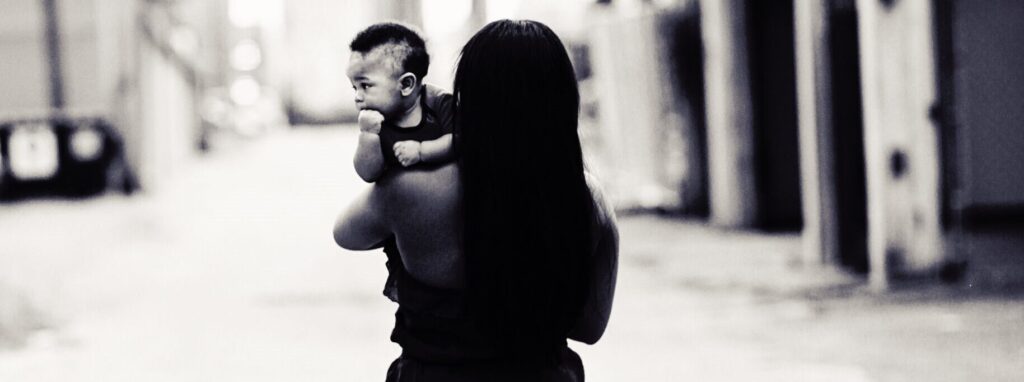 Mother in a blue dress holding her baby outdoors, celebrating motherhood and support through Hope Clinic for Women.